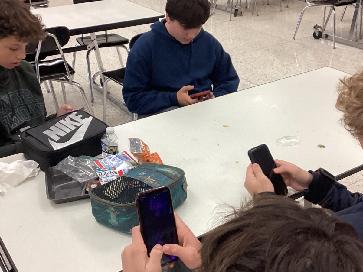 Students sit in the cafeteria looking at their phones during lunch.  Many students use their phones during lunch since they are not allowed to use them throughout the school day during class. 